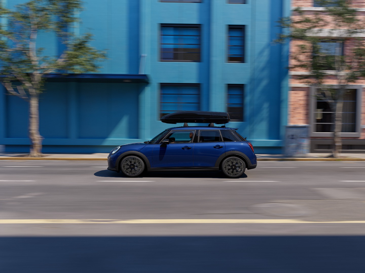 Three quarter front view of MINI Aceman in Indigo Sunset Blue equipped with MINI Roof Rack, carrying a MINI Roof Box 320. 